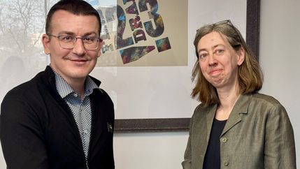 Sergiy Tomilenko, wearing a black cardigan, shakes hands with Laura Davison, wearing a grey blazer.