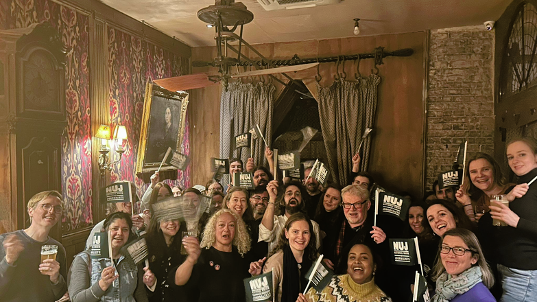 People smiling and holding green NUJ flags in a celebratory fashion.
