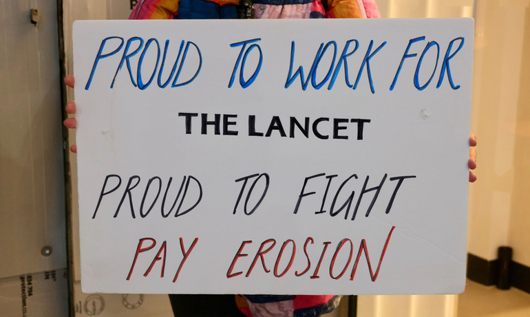 A white placard that says 'Proud to work for The Lancet, Proud to Fight Pay Erosion'