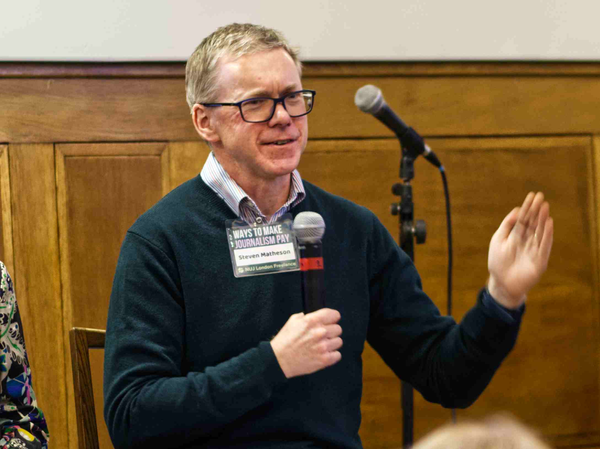 Steven Mathieson wearing a jumper and glasses speaking with a microphone.