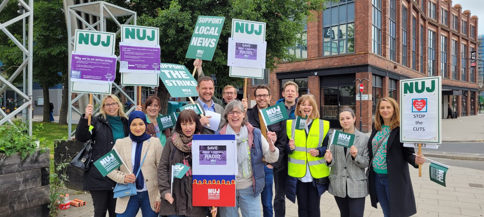 Picket line with placards outside BBC Leeds with large group smiling