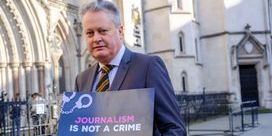 Vincent Kearney wearing a suit and tie holds a 'Journalism Is Not A Crime' placard.