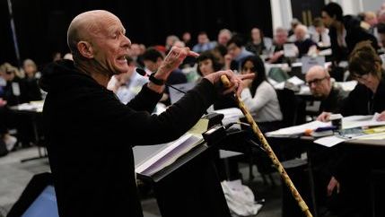 Eamonn McCann wearing a black sweatshirt and holding a walking stick speaks at DM 2025.