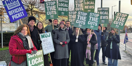 NUJ members stand on a picket line outside STV Glasgow HQ holding green 'Stop The Cuts' and 'Support Local News' placards.
