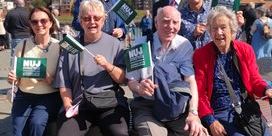 Members of the Sunderland, Shields and Hartlepool branch pose outside the river Wear with green NUJ flags with cloudy blue skies in the background.