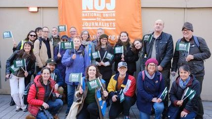 NUJ members pose behind an orange union banner outside parliament.