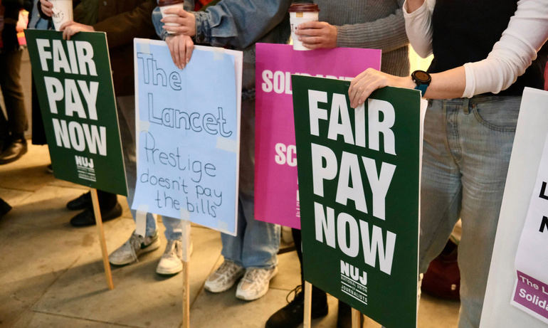 Hands holding green 'Fair Pay Now' placards and pink 'Solidarity for Science' placards.