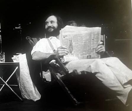 Black and white photo of John Mathews sitting in a chair and reading a broadsheet newspaper.