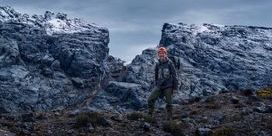 Klaus Thymann wearing hiking gear standing in front of mountainous, snow-topped rocks against a dark grey sky.