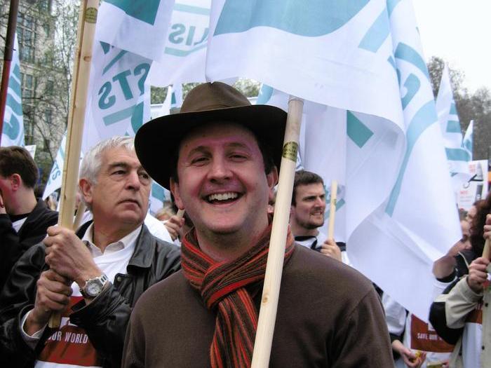Jonathan Lovett wearing a hat and scarf while holding an NUJ banner.