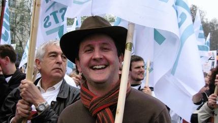 Jonathan Lovett wearing a hat and scarf while holding an NUJ banner.