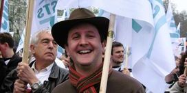 Jonathan Lovett wearing a hat and scarf while holding an NUJ banner.