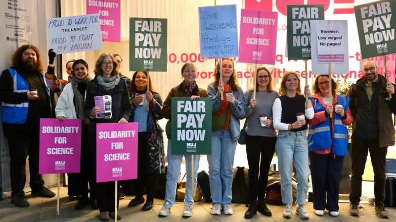 A group of people holding placards that say 'Fair Pay Now' and 'Solidarity for Science' with a glass building.