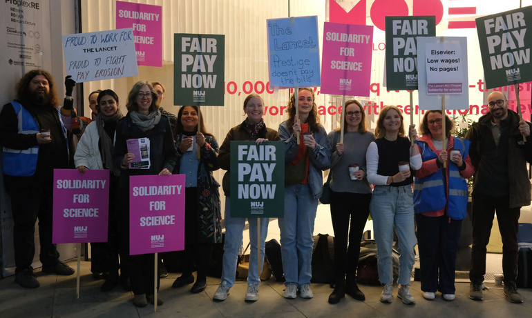 A group of people holding placards that say 'Fair Pay Now' and 'Solidarity for Science' with a glass building.