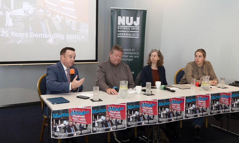 Four people seated on a panel with a man holding a microphone, and a projection and green NUJ banner in the background.