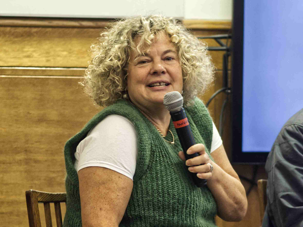 Eleanor Mills wearing a grey cardigan holding a microphone.