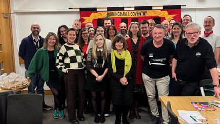People standing and smiling in an office room in front of a red NUJ banner.