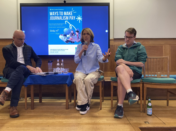 Grace Livingstone holding a microphone and gesturing while wearing a pale blue shirt with two men seated either side.
