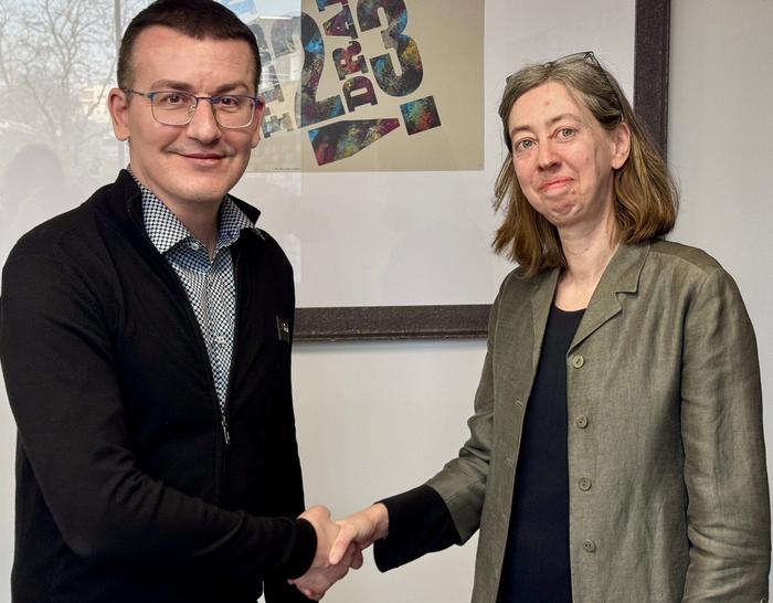 Sergiy Tomilenko, wearing a black cardigan, shakes hands with Laura Davison, wearing a grey blazer.