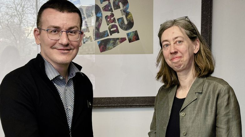 Sergiy Tomilenko, wearing a black cardigan, shakes hands with Laura Davison, wearing a grey blazer.