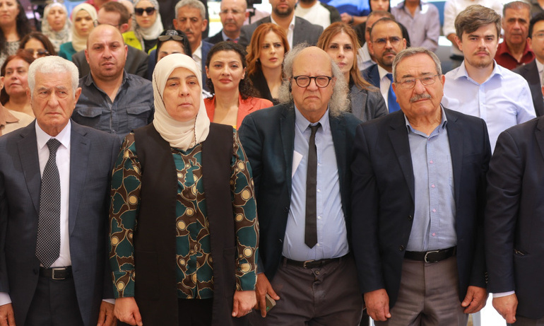 Attendees at the unveiling event pose for a picture. Men in the front row wear dark suits and ties, a woman wears a light coloured hijab.