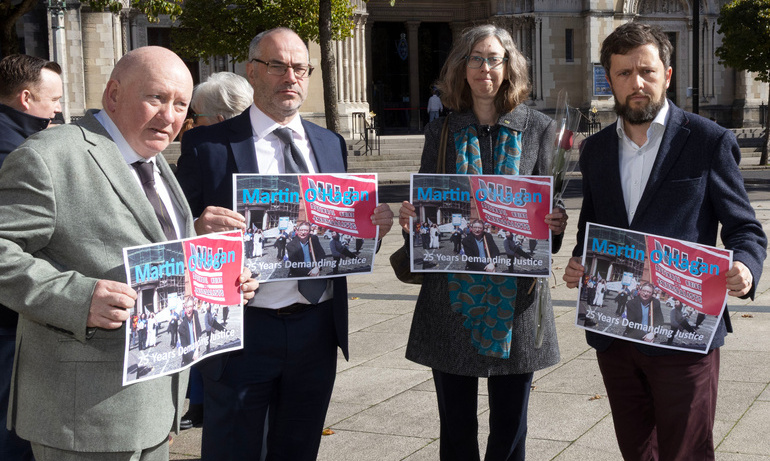 Séamus Dooley, Patrick Corrigan, Laura Davison wearing suits and coats and holding posters depicting Martin O'Hagan.