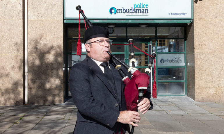 A piper wearing traditional dress plays outside the Police Ombudsman of Northern Ireland office.