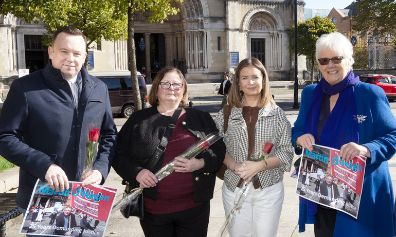 Fran McNulty, Tina O'Hagan, Niamh O'Hagan, and Anne Hailes holding posters and flowers on a square with a church entrance in the background.