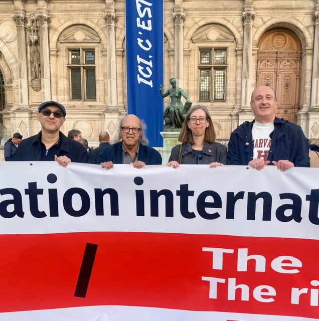 Four people stand behind a red and white banner in Paris.