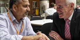 Barnie Choudhury and John McDonnell sitting at a table and shaking hands.