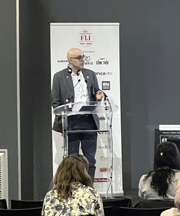 Hanif Mazrooei wearing a black suit speaking behind a lectern.