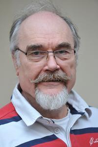 Chris wears striped shirt, clear spectacles as he smiles for a photo.