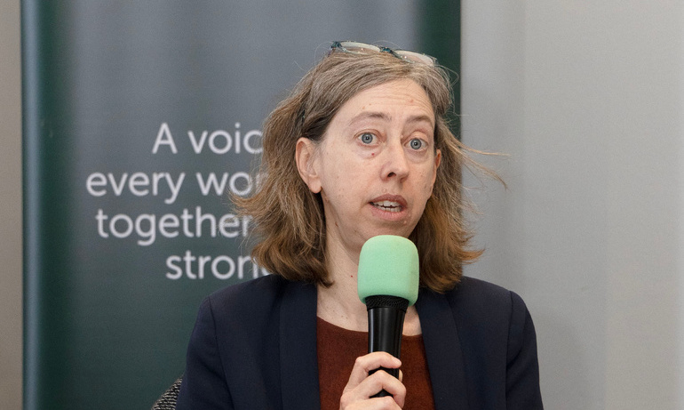 Laura Davison holding a microphone with the words 'Demanding Justice' projected onto a screen behind her.